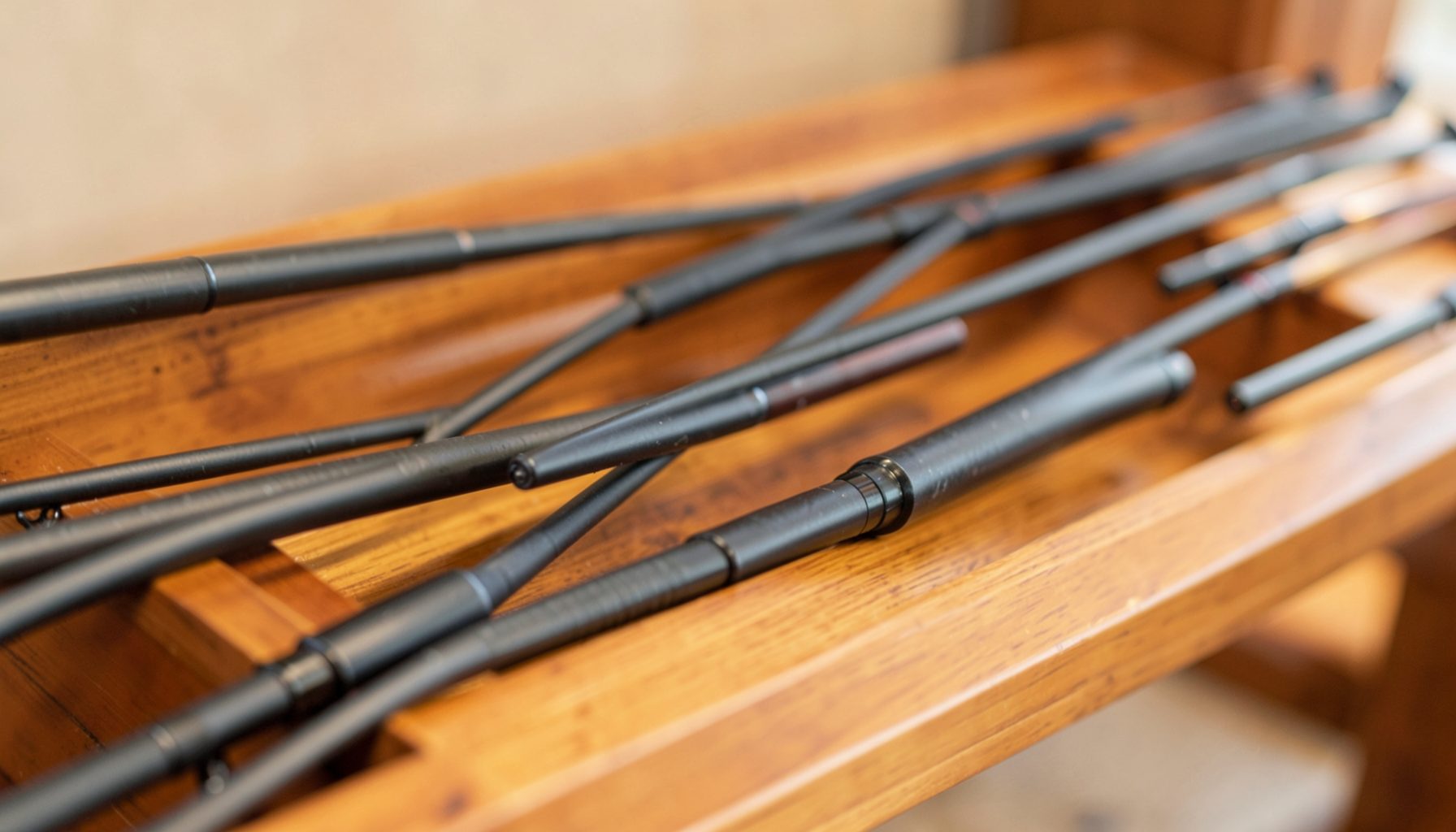 Close-up of several black fishing rod sections crossing on a polished wooden surface, warm brown tones